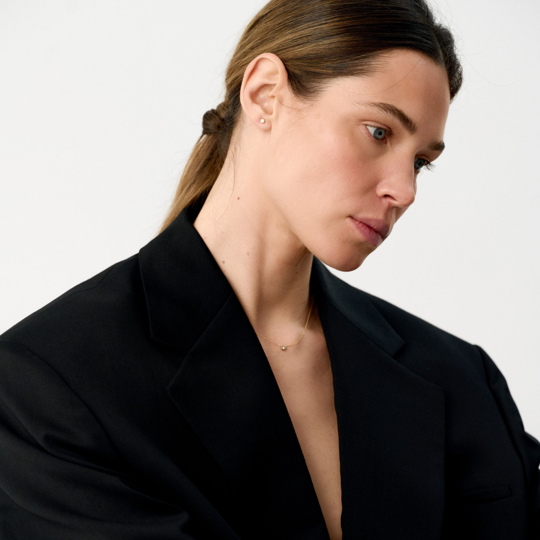 Woman wearring yellow gold pendant and earrings featuring a round brilliant-cut diamonds.