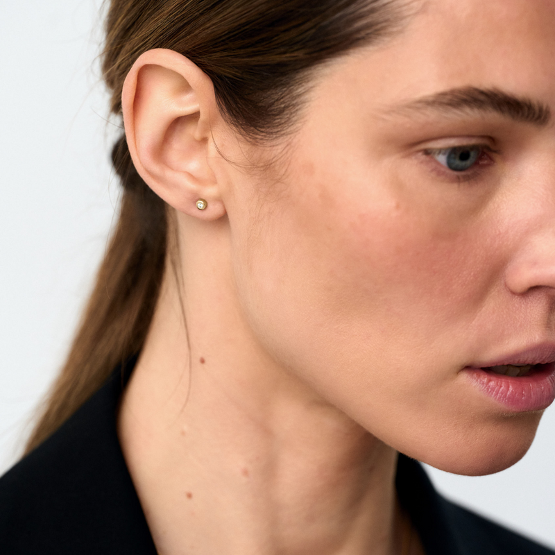 Close-up of a woman wearing a small gold & diamonds stud earring with a plain background
