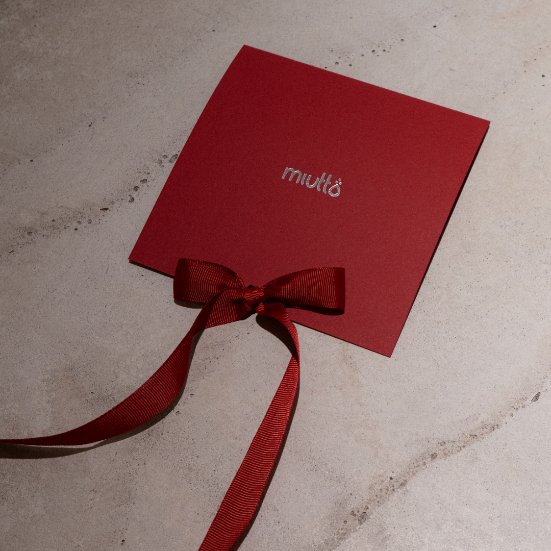 Red card with a bow on a textured surface, featuring the brand 'miutto'.