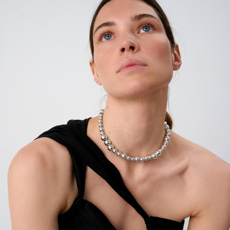 Woman wearing a statement necklace crafted from fine sterling silver beads in varying sizes. 