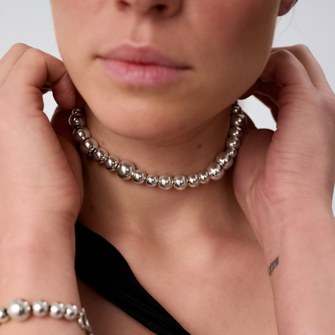 Woman wearing a statement necklace crafted from fine sterling silver beads in varying sizes. 