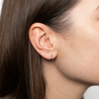 Close-up of a person wearing white gold hoop earring with a plain background