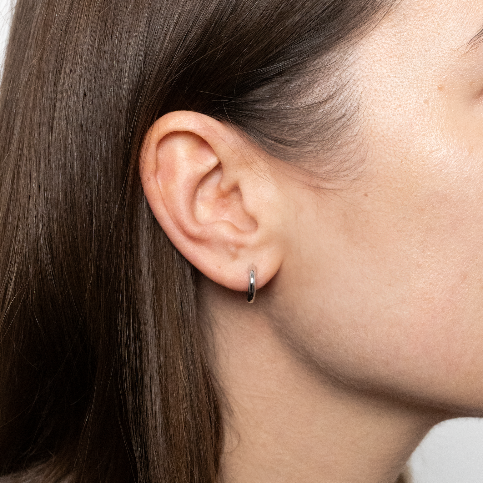 Close-up of a person wearing white gold hoop earring with a plain background