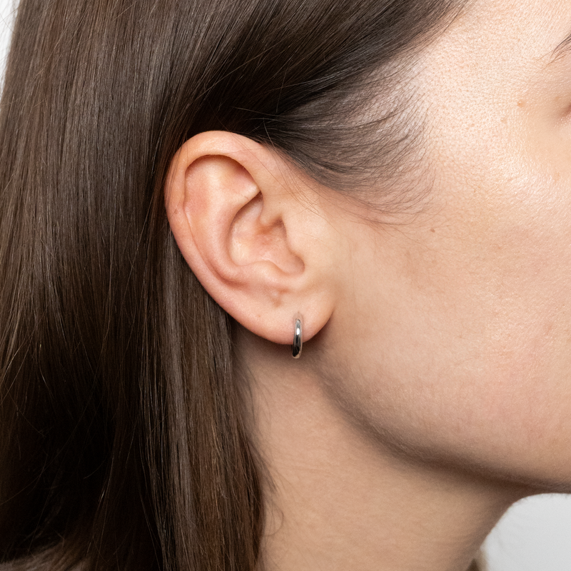 Close-up of a person wearing white gold hoop earring with a plain background