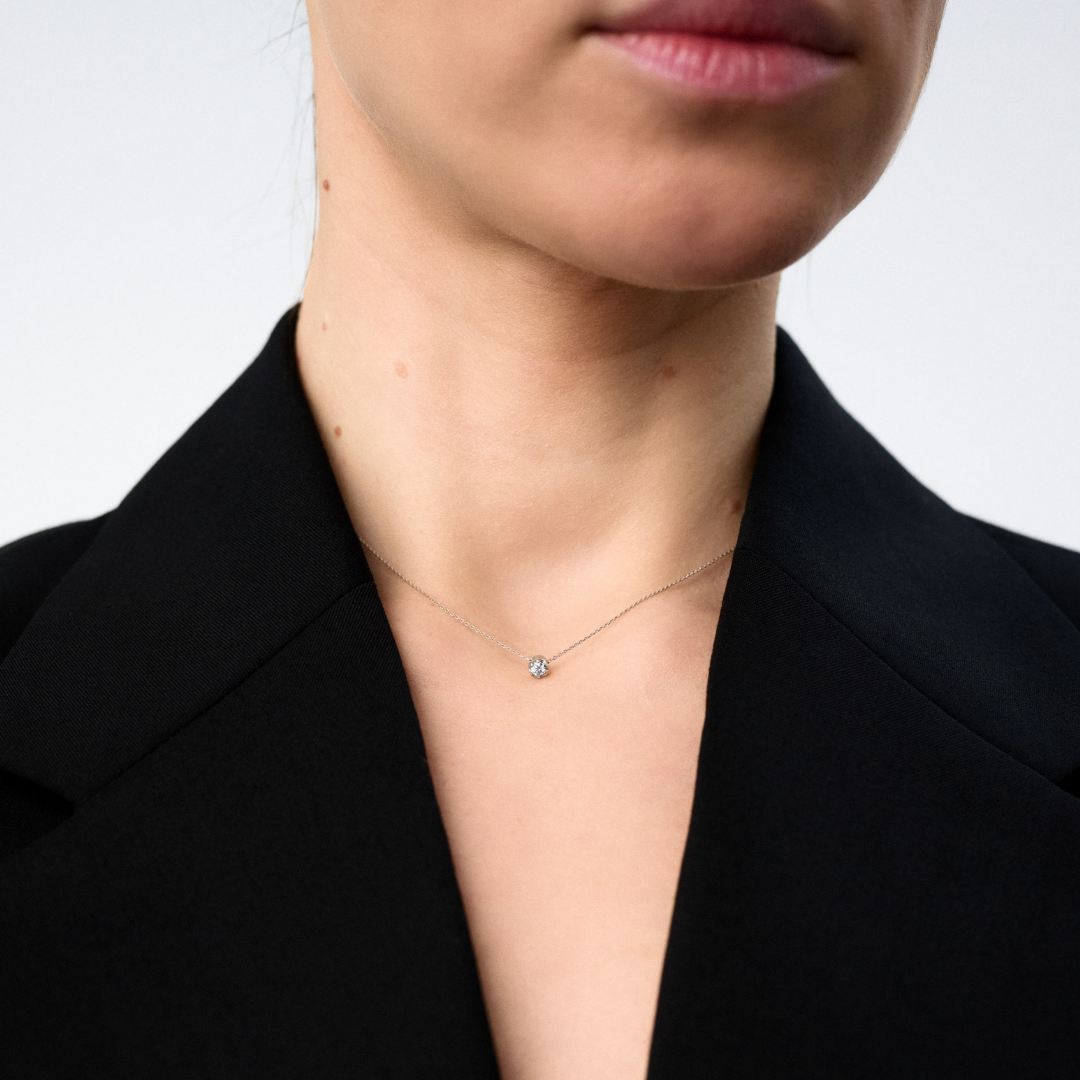 Woman wearing a white gold pendant featuring a round brilliant-cut diamond, suspended from a delicate gold chain. 