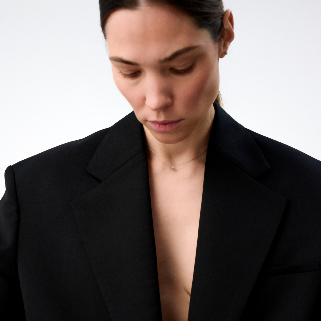 Woman wearing a white gold pendant featuring a round brilliant-cut diamond, suspended from a delicate gold chain. 