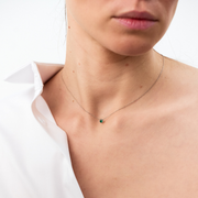 Woman wearing a white gold pendant featuring a round emerald, suspended from a delicate gold chain. 