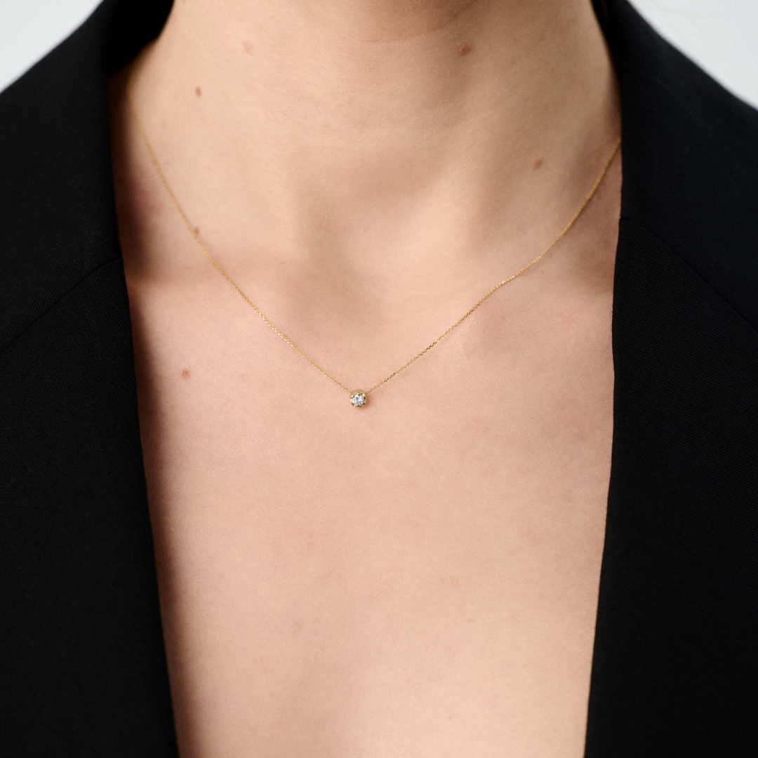 Woman wearing a yellow gold pendant featuring a round brilliant-cut diamond, suspended from a delicate gold chain. 