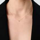 Woman wearing a yellow gold pendant featuring a round brilliant-cut diamond, suspended from a delicate gold chain. 