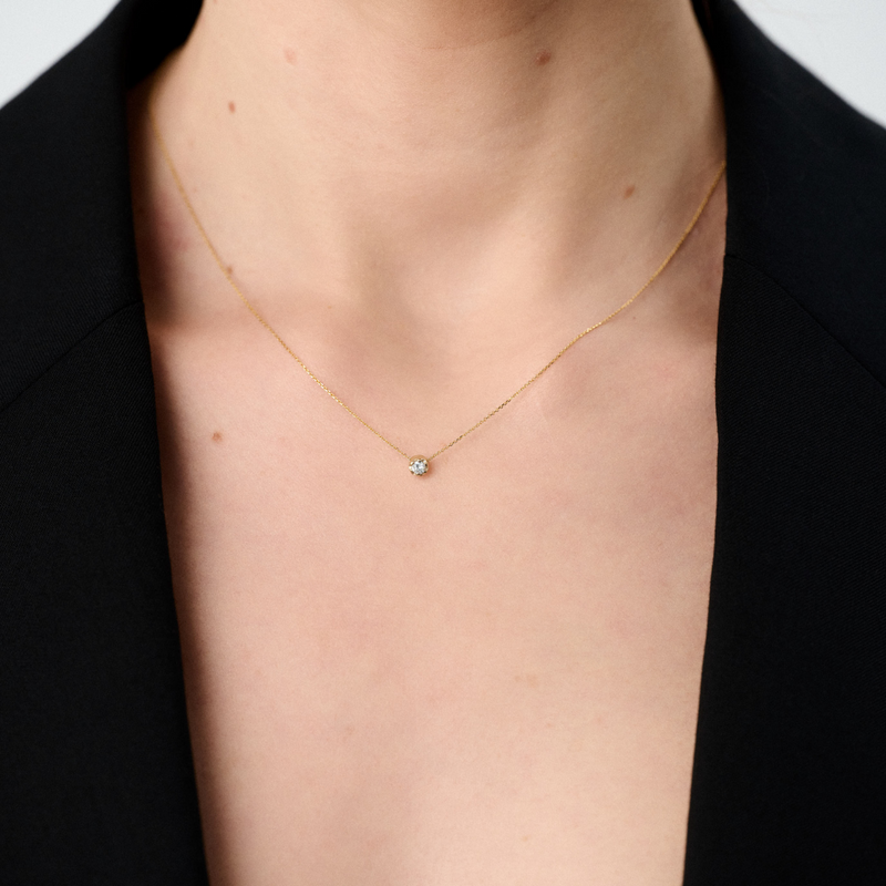 Woman wearing a yellow gold pendant featuring a round brilliant-cut diamond, suspended from a delicate gold chain. 