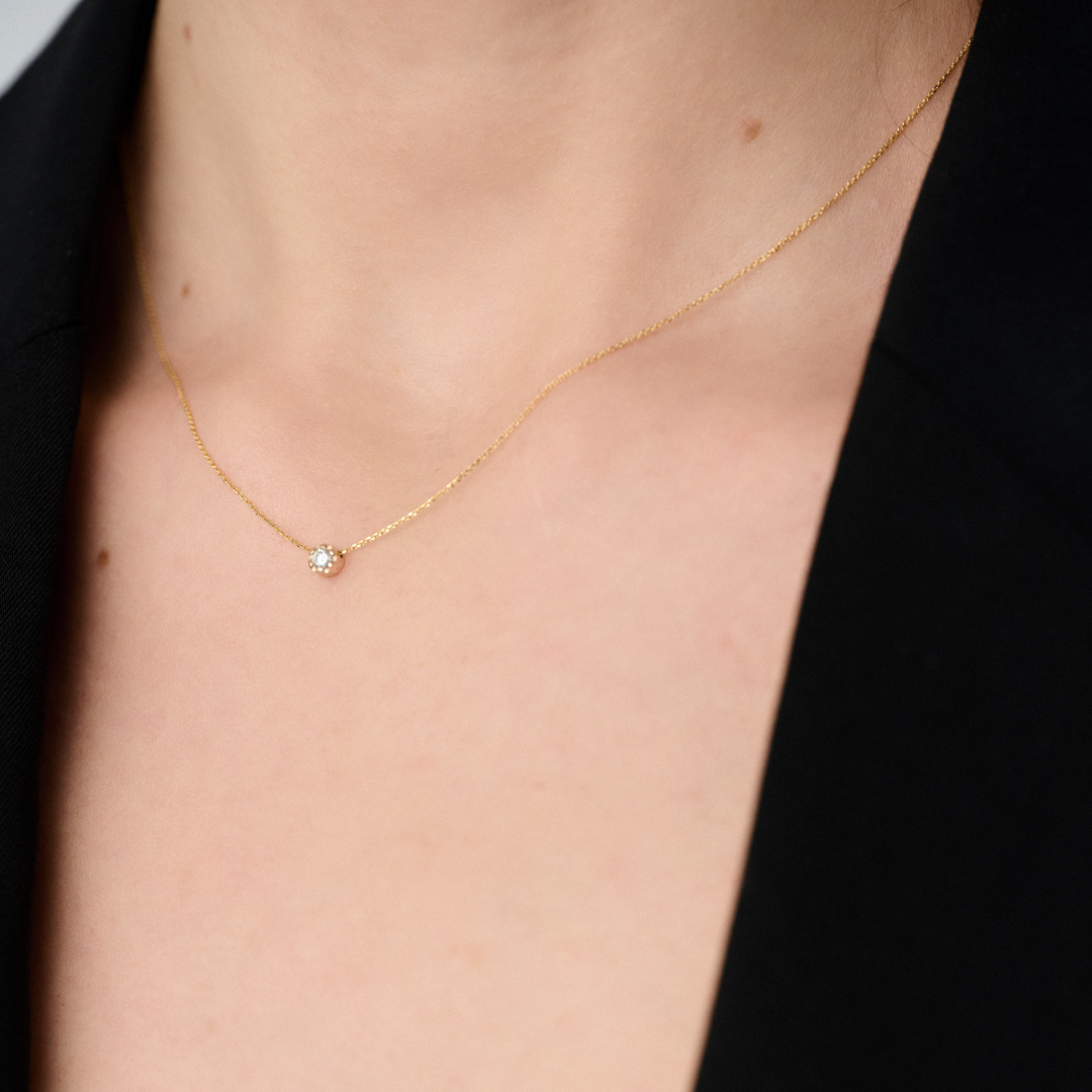 Woman wearing a yellow gold pendant featuring a round brilliant-cut diamond, suspended from a delicate gold chain. 