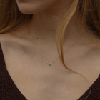 Yellow gold pendant featuring a round emerald, suspended from a delicate gold chain on a person's neck.