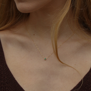 Yellow gold pendant featuring a round emerald, suspended from a delicate gold chain on a person's neck.