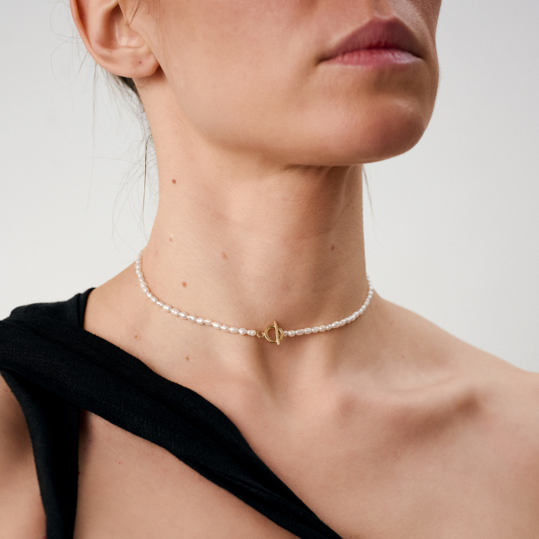 Woman wearing a delicate freshwater pearl necklace featuring organically shaped pearls and a minimalist yellow gold clasp.