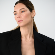 Woman wearing a minimalist necklace featuring a pear-cut diamond set on a fine 14k yellow gold chain.