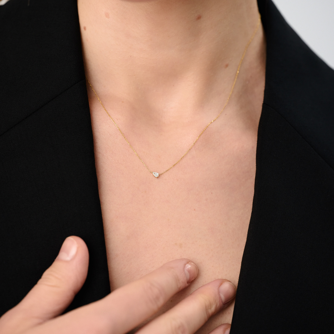 Woman wearing a minimalist necklace featuring a pear-cut diamond set on a fine 14k yellow gold chain.