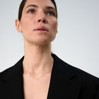 Woman wearing a minimalist necklace featuring a pear-cut diamond set on a fine 14k yellow gold chain.