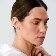 Woman wearing stud earrings featuring round emeralds set in 14k yellow gold.