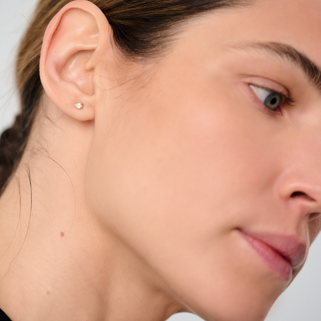 Woman wearing minimalist stud earrings featuring pear-cut diamonds set in 14k yellow gold.&nbsp;