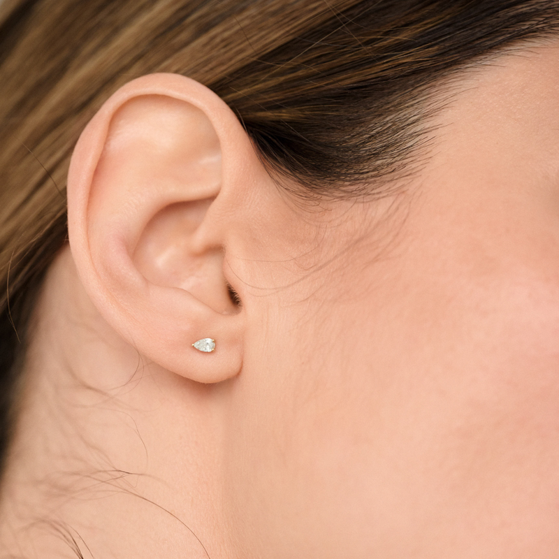 Woman wearing minimalist stud earrings featuring pear-cut diamonds set in 14k yellow gold.