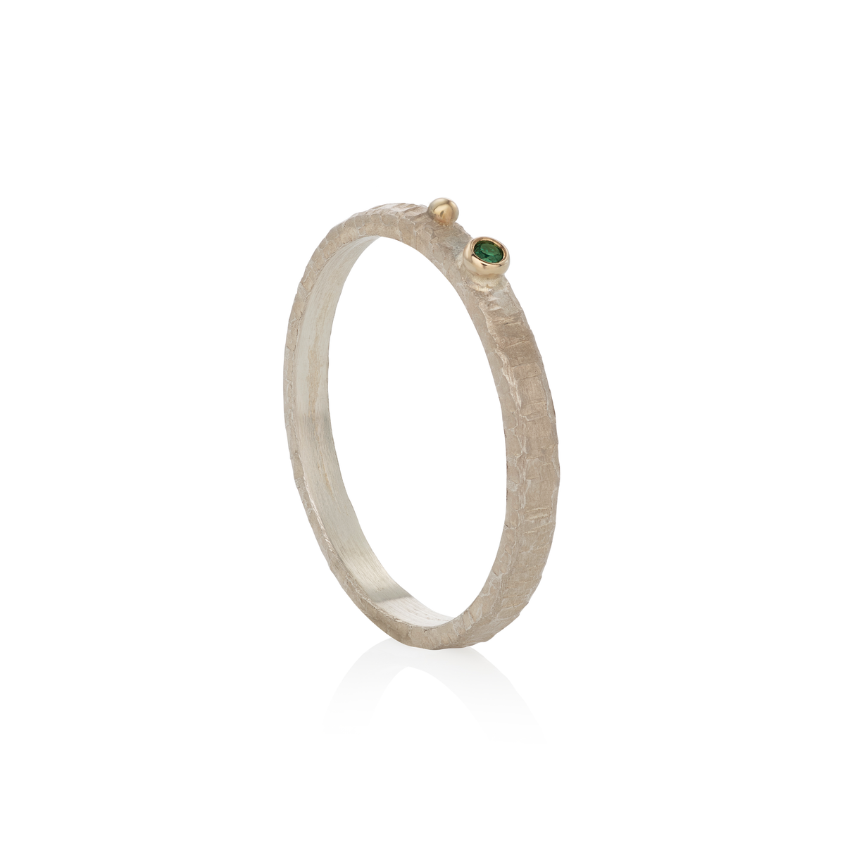 A textured silver ring with a small gold bead accent and a tiny green emerald on the side, shown on a clean white background.