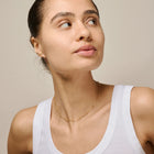Woman wearing a white tank top and gold necklace against a beige background