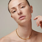 Woman wearing a gold necklace against a neutral background