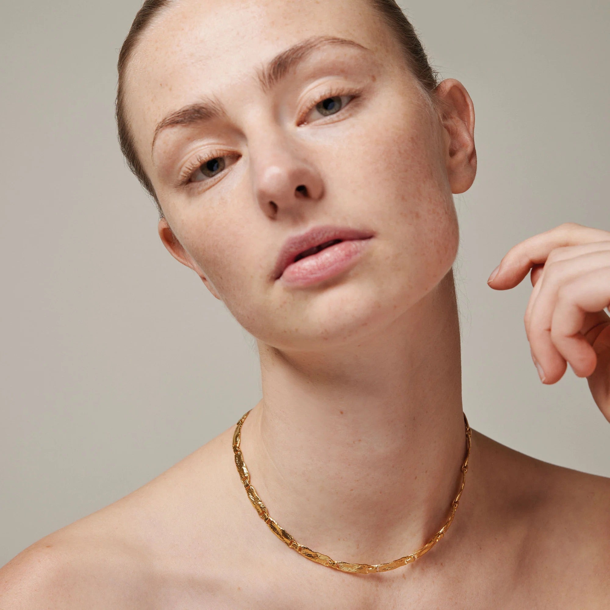 Woman wearing a gold necklace against a neutral background