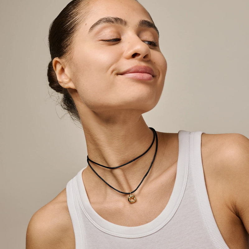 Woman wearing a white tank top and black necklaces with a gold pendant on a beige background