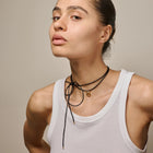 Woman wearing a white tank top and multiple necklaces against a neutral background