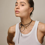 Woman wearing a white tank top and multiple necklaces against a neutral background