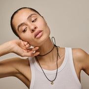 Woman wearing a white tank top and black necklace against a beige background