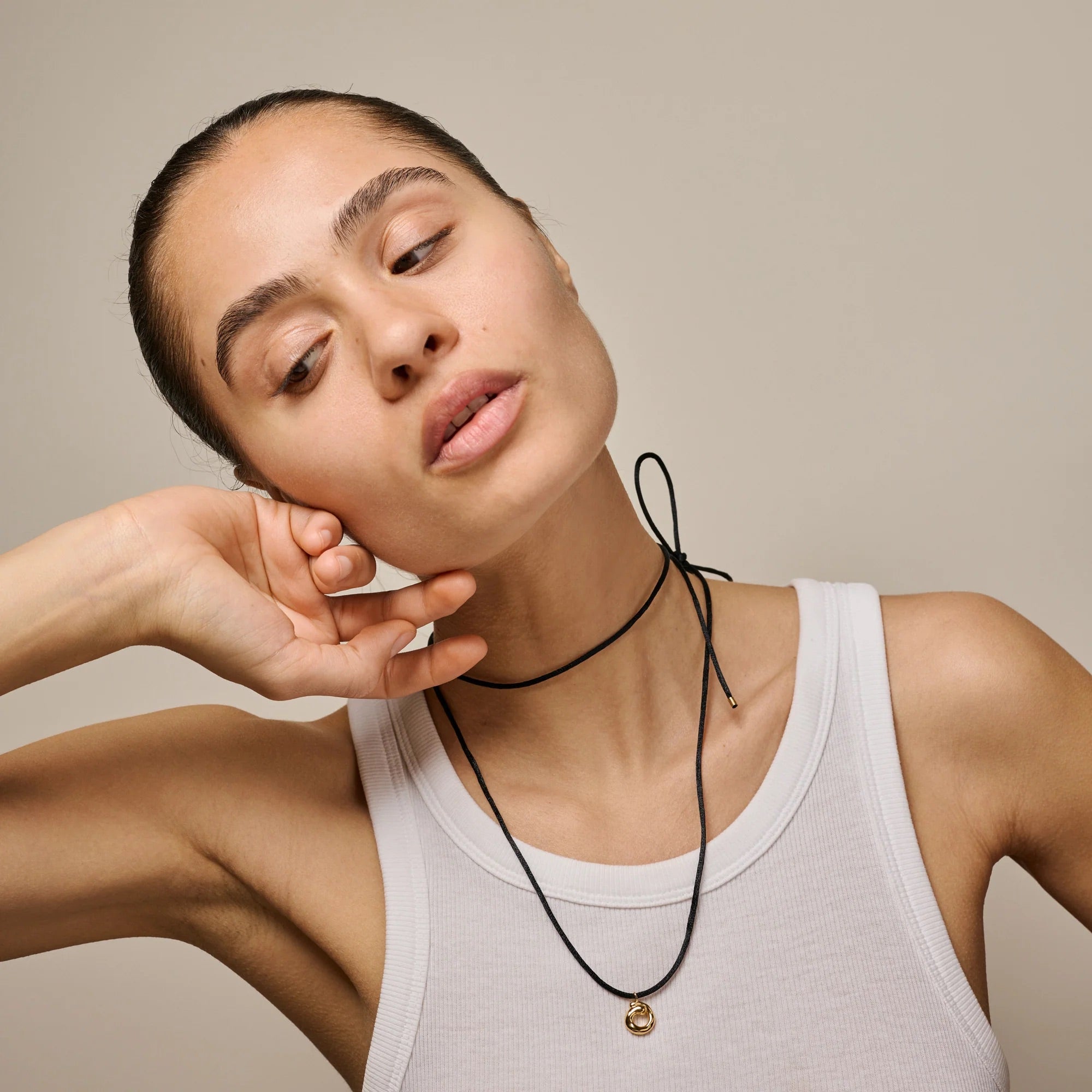 Woman wearing a white tank top and black necklace against a beige background