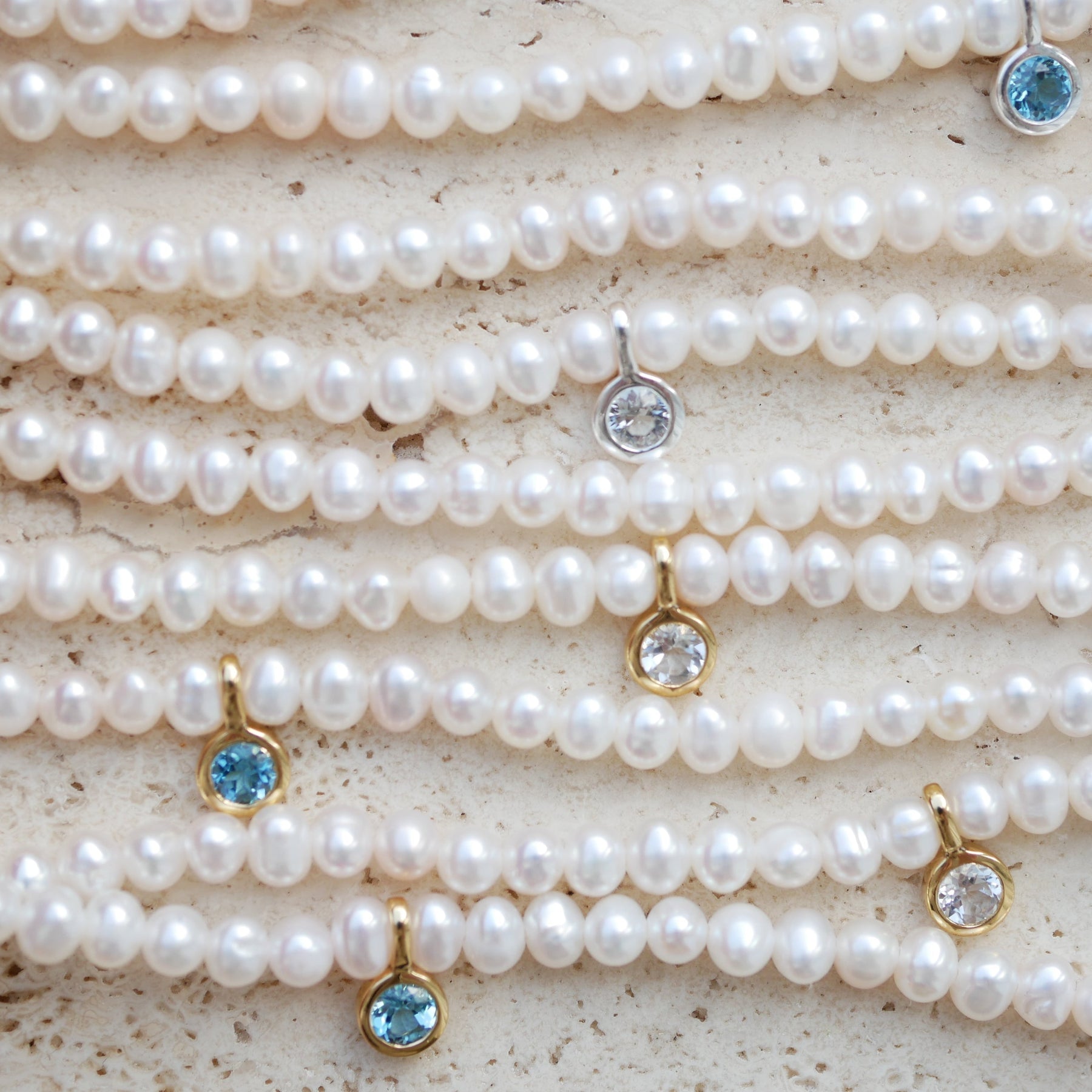 Pearl necklaces with topaz gemstone pendants on a textured surface