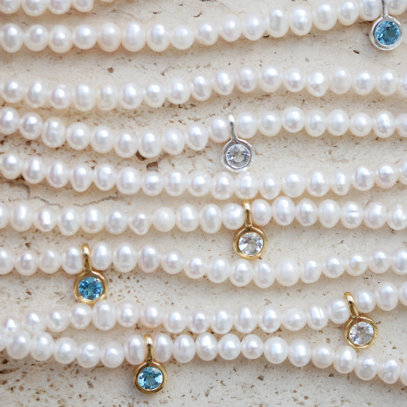Pearl necklaces with topaz gemstone pendants on a textured surface