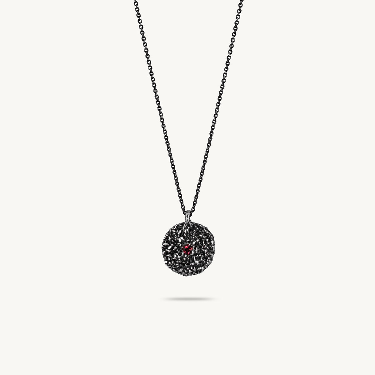 Oxidised silver chain necklace featuring a round, textured disc pendant with a small red sapphire set in the center