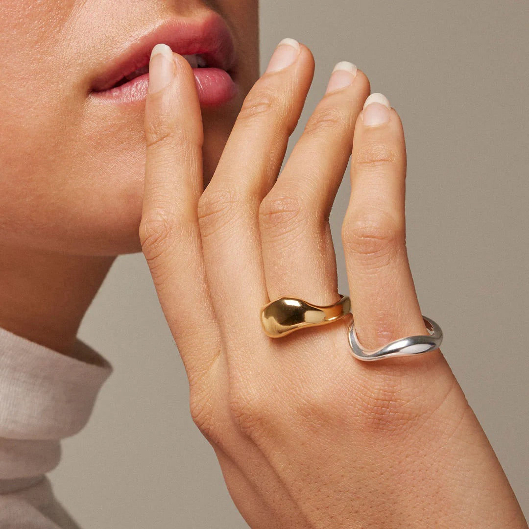Close-up of a hand with two rings, one gold and one silver, on a neutral background.