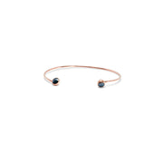 A delicate gold open cuff bracelet with a small dark blue faceted diamonds set in each end, shown on a plain white background.