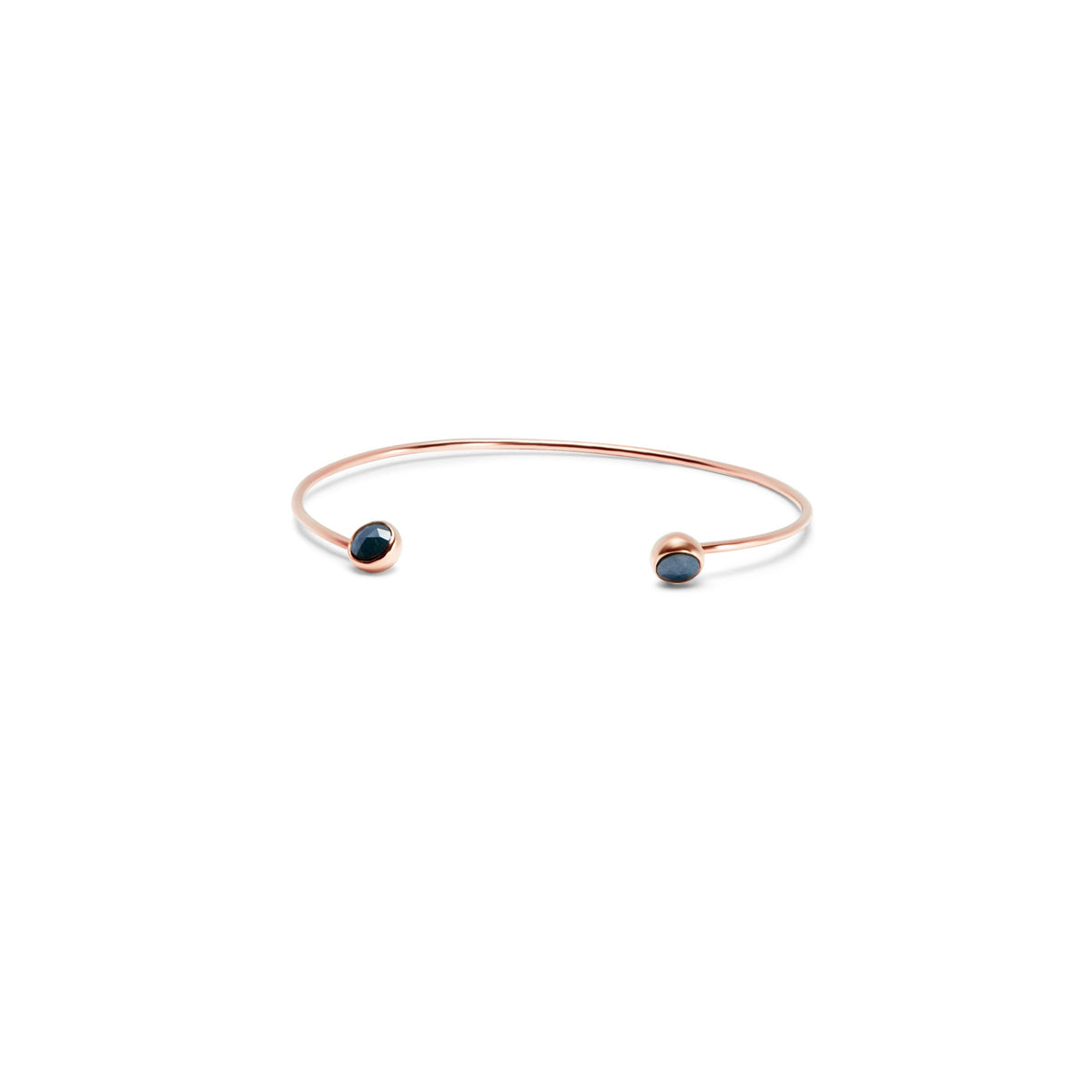 A delicate gold open cuff bracelet with a small dark blue faceted diamonds set in each end, shown on a plain white background.