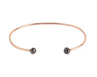 A thin rose gold open cuff bangle bracelet with two small faceted grey diamonds at the ends, shown on a plain white background.