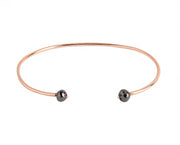A thin rose gold open cuff bangle bracelet with two small faceted grey diamonds at the ends, shown on a plain white background.