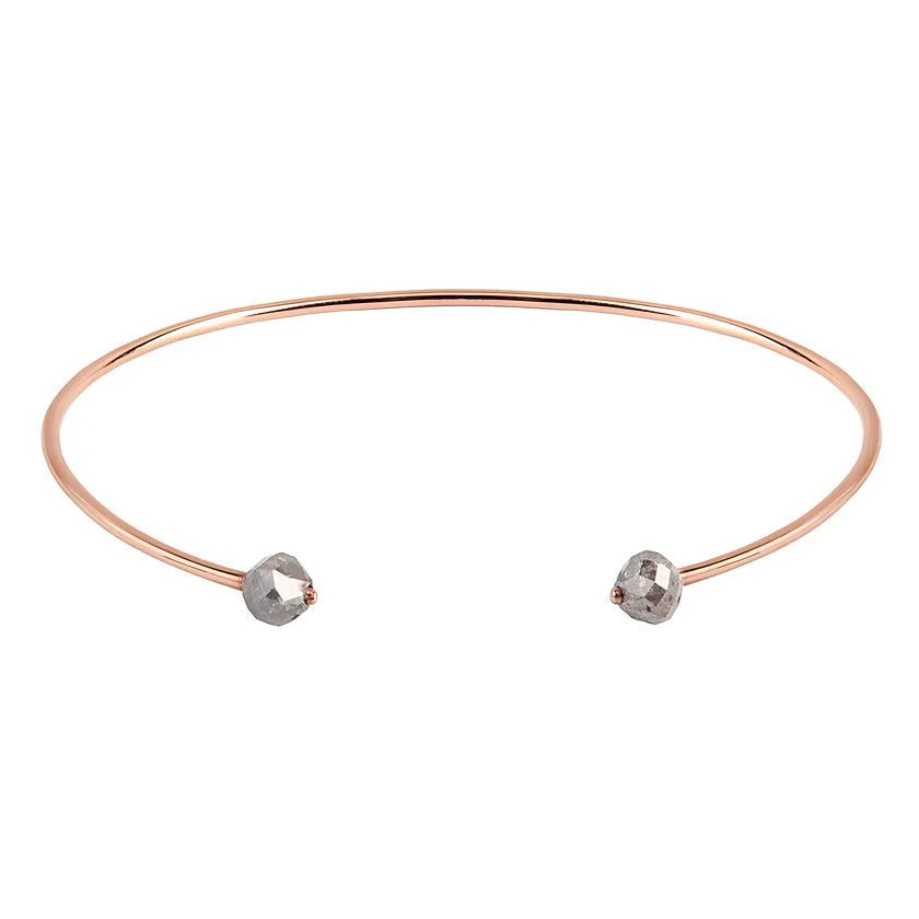A thin rose gold open cuff bangle bracelet with two small faceted grey diamonds at the ends, shown on a plain white background.