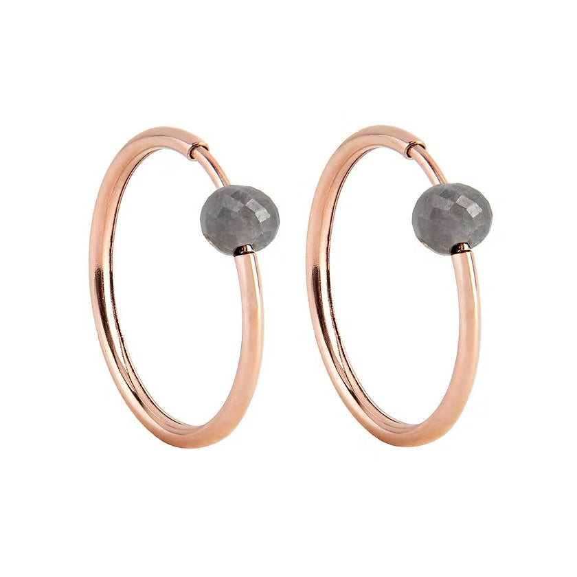 A pair of rose gold hoop earrings with a small, faceted dark grey diamond bead attached near the top right of each hoop, shown against a plain white background.