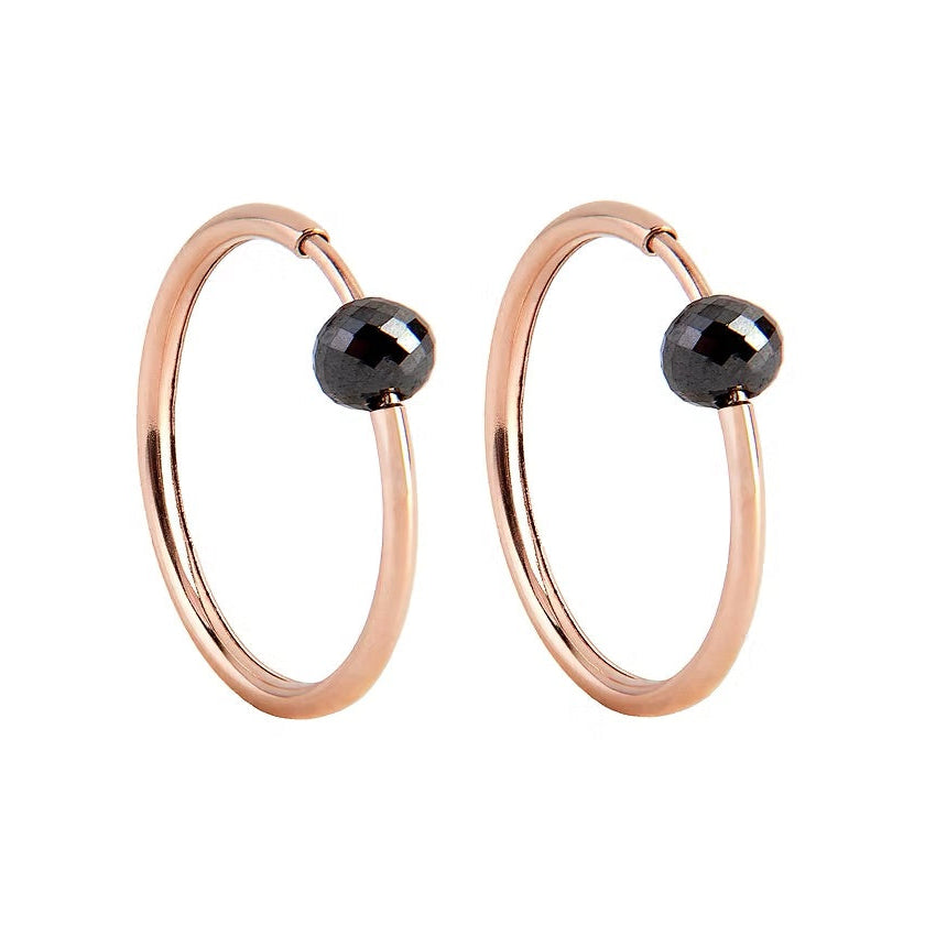 A pair of rose gold hoop earrings with a small, faceted black diamond bead attached near the top right of each hoop, shown against a plain white background.