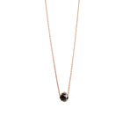 A delicate rose gold chain necklace with a small, faceted black gemstone pendant, shown against a plain white background.