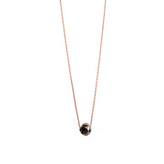 A delicate rose gold chain necklace with a small, faceted black gemstone pendant, shown against a plain white background.