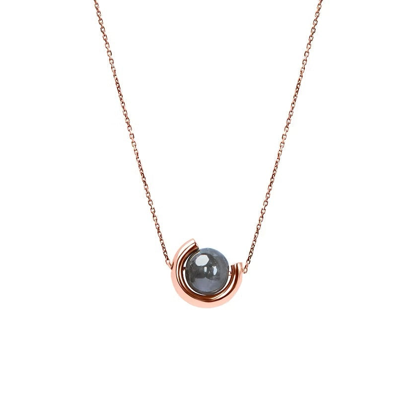 A delicate rose gold chain necklace featuring a unique crescent-shaped gold pendant cradling a smooth, dark grey diamond, shown against a solid white background.