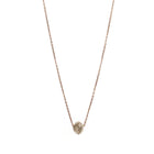A delicate rose gold chain necklace featuring a small, raw, faceted diamond pendant, shown against a solid white background.