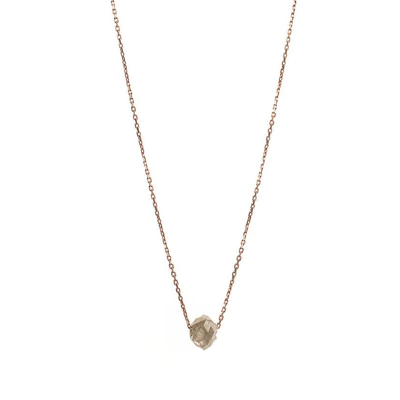 A delicate rose gold chain necklace featuring a small, raw, faceted diamond pendant, shown against a solid white background.
