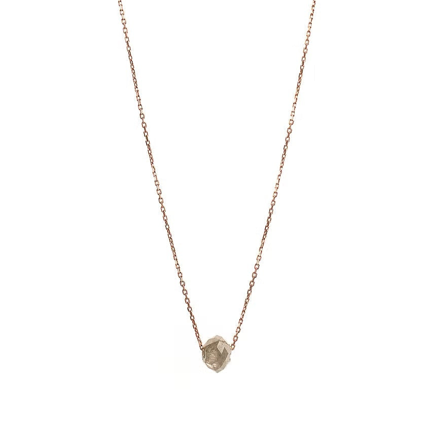 A delicate rose gold chain necklace featuring a small, raw, faceted diamond pendant, shown against a solid white background.